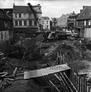 Firma Carl Hoffmann: Hindenburgstraße: Elektrohandel: Neubau: Fundament: Blick in Baugrube mit Holzverschalungen, Brettern und Bagger: hinten Wohn- und Geschäftshäuser mit Drogerie Purnhagen: hinten Mitte Rathaus, Stadthaus und eingerüstetes Gebäude