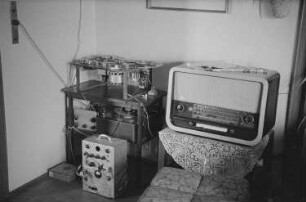 Zimmeransicht mit einem Tonbandgerät (?) und einem Röhrenradio