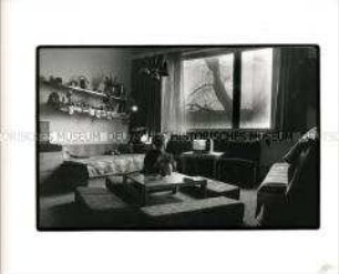 Blick in ein Wohnzimmer mit der Rückenansicht einer Person die auf einen Fernseher schaut (Altersgruppe 14-17)
