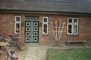 Fritz-Berodt-Straße 6: traufständiges Bauernhaus aus Backstein: Straßenfront: Teilansicht: Eingangstür mit Oberlicht, Fenster: vor Außenmauer Ruhebank