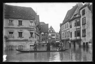 Hochwasser in der Brückengasse Richtung Marktplatz vor Chorstift-Drogerie F. Schwender, Jakob Beysel, Pelz- und Modewaren Johanna Strauß u.a. sowie Brunnen, darauf Personen in Schelchen