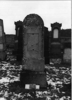 Grabstein 16 (Index: 100114965) Zustand: zerbrochen und repariert, Texttafel fehlt Maße HxBxT: 187x54x24 cm Beschreibung: Stele auf gestuftem Sockel, Rundbogen mit Korb und Rosenblüten, eingesetzte Texttafel Symbolik: Korb mit Rosenblüten: Grabstein 16
