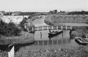 Glashauslandschaft-Westerland : Blick über eine Landschaft mit einem kleinen Kanal, Booten, einer Brücke und Gewächshäusern