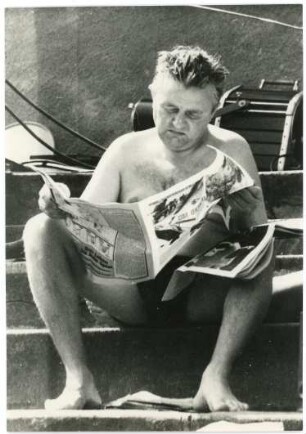 Mann im Freibad sitzend und Zeitung lesend