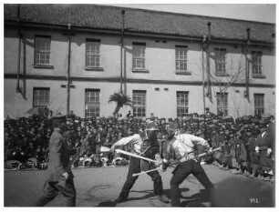 Nagasaki. Zwei japanische Soldaten beim Fechtkampf vor Zuschauern. Blick gegen eine Kaserne
