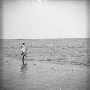 Fischer : Ein Fischer geht mit einem Wurfnetz am Strand entlang.