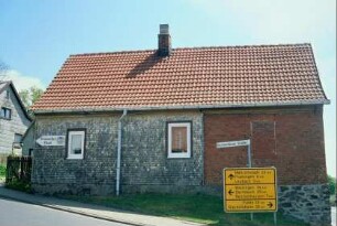 einstöckiges Wohnhaus, davor Wegweiser