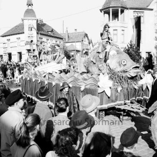 Karpfenfest: Umzug: Bahnhofstraße, hinten Mitte Einmündung von Bischofsteicher Weg: Festwagen, Fischerin mit Kescher reitet auf Riesenkarpfen, dahinter Fischerinnen in Boot: umgeben von Zuschauern, 13. Oktober 1957