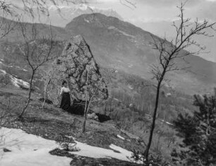 Frau an einem Findling : Eine Frau vor einem Findling in einer verschneiten Landschaft. Im Hintergrund hohe Berge