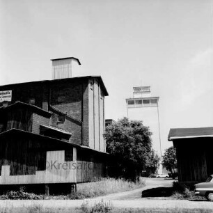Mühlenbetrieb W. F. Stoltenberg: rechts und links Gebäude: im Hintergrund der neue Silo: davor Bäume: vorn Gleise
