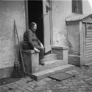 Alte Frau an einem Treppenaufgang sitzend