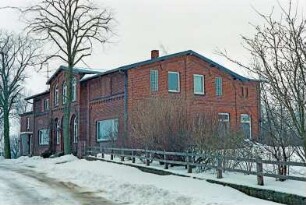 Hamannsöhlen: traufständiges Bauernhaus aus Backstein: Straßenfront mit Eingangsrisalit, Bogenfenster, Panoramafenster, hinten links Anbau mit Tür: Giebelseite, rechts rückwärtiger Anbau: zwei Bäume, Gartenzaun: Schnee