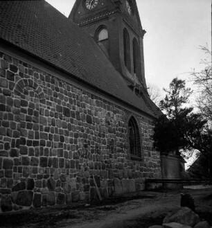 Martin-Luther-Kirche: Außenansicht: vor Sockel Erdarbeiten: hinten rechts Eisenträger an Wand: darüber kleines Holzgerüst auf Dach: hinten Bäume
