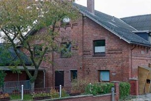 Fritz-Berodt-Straße 5: traufständiges Bauernhaus aus Backstein: Giebelseite ehemaliger Wirtschaftstrakt mit Umbauten, Tür, links flacher Anbau: rechts Straßenfront [angeschnitten] mit Eingangstüren, Windfang: Garten, Gartenmauer, Obstbaum