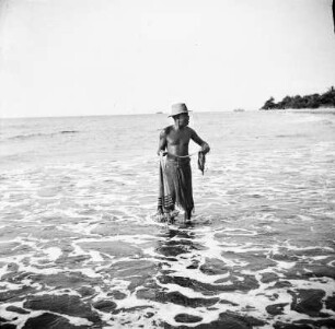 Fischer : Ein Mann fischt mit einem Wurfnetz nahe des Strandes.