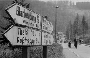 Wegweiser in Treseburg, Wanderer auf der Straße, im Hintergrund Berglandschaft