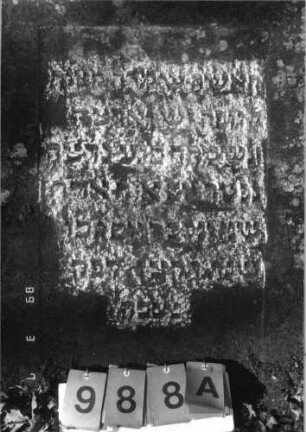 Grabstein 988 (Index: 99751362) Material: Sandstein Zustand: stark verwitt. /Textverlust Maße HxBxT: 109x65x9 cm Beschreibung: eingezog. Rundbogenabschl. , gekappte Pyramiden als Eckakrotere, Schrift eingetieft Symbolik: Blüte: Grabstein 988A