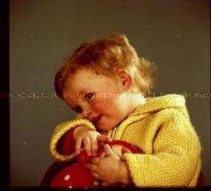Kleines Mädchen mit Strickjacke und Puppe