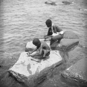 Jungen am Strand : Zwei Jungen schlagen gesammelte Muscheln auf einem Stein auf.