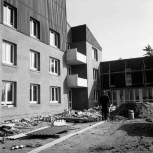 Wohnheim für Behinderte der Ahrensburger Werkstätten [später Stormarner Werkstätten Ahrensburg]: Langeneßweg: Träger Evangelisches Diakonisches Werk in Rendsburg: in Bau: Fenster eingesetzt: rechts seitlicher Anbau mit Gerüst: Arbeiter mit Schubkarre auf Holzplanken: Erdhaufen, Bauschutt, Wellblech