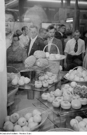 Besucher mustern ausgestelltes Obst der indischen Sektion auf der Leipziger Herbstmesse 1954