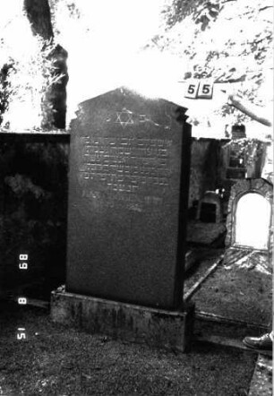 Grabstein 55 (Index: 100105518) Material: Granit Zustand: gut Maße HxBxT: 174x74x19 cm Beschreibung: Stele, Sockel, gezackt eingezogener giebelartiger Abschluß Symbolik: Davidstern Besonderheit: möglicherweise Doppelgrab, die Einfassung umfaßt zwei Plätze: Grabstein 55
