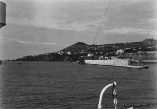 Hafenmauer : Eine Mole vor der brasilianischen Küste von einem Schiff aus fotografiert. Im Hintergrund die Häuser einer Stadt.
