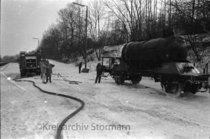 Bahnhof: Übung der Bahnfeuerwehr Lübeck mit Freiwilliger Feuerwehr Reinfeld: rechts Kesselwagen auf Gleis: vorn Schlauch: hinten Löschfahrzeug, Feuerwehrleute und Beobachter: dahinter Böschung mit Bäumen: Winter