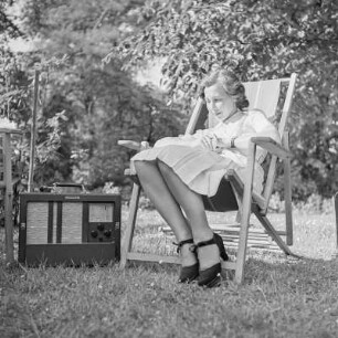 Elisabeth Gremmler sitzt in einem Klappstuhl im Garten, neben ihr steht ein Rundfunkempfänger