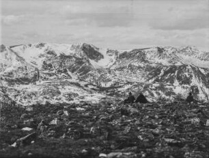 Bergpanorama : Eine Berglandschaft mit verschneiten Gebirgszügen im Hintergrund. Im Vordergrund sitzen drei Mitglieder des Transkontinentalen Geographenkongresses