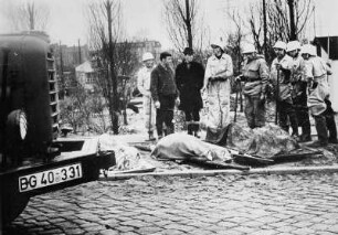 Hamburg. Im Stadtteil Wilhelmsburg liegen geborgene Opfer der Flutkatastrophe am Straßenrand. Helfer stehen daneben.