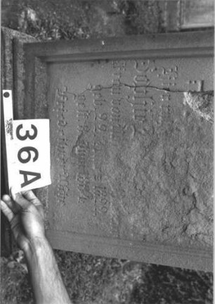 Grabstein 36 (Index: 99808466) Material: Sandstein Zustand: stark verwittert, beschädigt, mit Textverlust Maße HxBxT: 195x62x32 cm Beschreibung: Stele, getreppter Sockel, giebelartiger Abschluß mit Verdachung und Eckakroteren, Schriftfeld eingetieft mit Rundbogenabschluß Symbolik: gestelztes Fries: Grabstein 36A