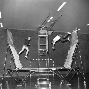 Trampolinspringen. Zwei Springer auf einem Trampolin mit links und rechts schräg angebrachten Seitentrampolins