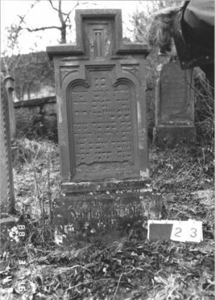 Grabstein 23 (Index: 100114488) Material: Sandstein Zustand: abgeblättert, Sockel verwittert Maße HxBxT: 146x62x19 cm Beschreibung: Stele, Sockel, getreppter Abschluß: Grabstein 23