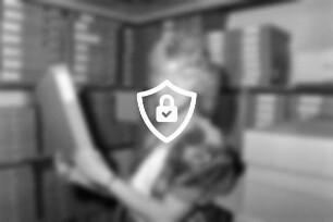 Mitarbeiterin [Name maskiert] vom Kreisarchiv steht vor Regalen mit Archivschachteln und hält eine davon in [Name maskiert]