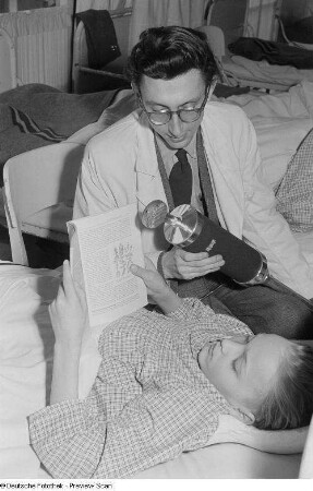 Ein Mann hält einem lesenden Kind ein Mikrofon im Dr.-Georg-Sacke-Heim