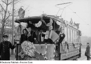 Musizierende Karnevalisten und Personal auf einer geschmückten Straßenbahn
