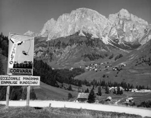 Corvara (Südtirol). Ortsteilansicht mit Ortshinweisschild auf einer Bergstraße