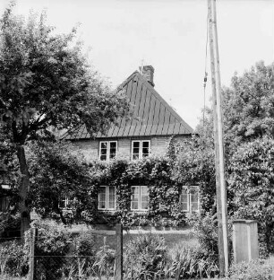 Bauernhaus von Heinz Lange: Giebelfront mit Rankgewächsen: davor Vorgarten mit Bäumen: vorn rechts Fahnenmast
