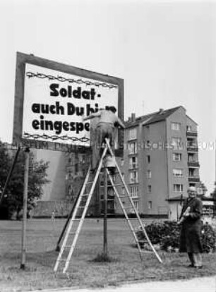 An der Westseite der Berliner Mauer werden Plakate Richtung Ost-Berlin aufgestellt