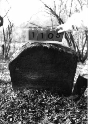 Grabstein 1105 (Index: 99753278) Material: Sandstein Zustand: verwitt/Textverl/Stele eingesunk/gekippt Maße HxBxT: 73x69x12 cm Beschreibung: Stele, Segmentbogenabschluß: Grabstein 1105