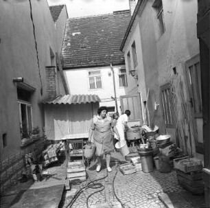 Hinterhof : Blick in einen Hinterhof, in dem drei Frauen in weißen Kittelschürzen Eimer und Körbe tragen