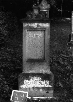 Grabstein 49 (Index: 100101019) Material: Sandstein, neue Platte Zustand: Schrifttafel fehlt, Sockel verwittert Maße HxBxT: 152x45x23 cm Beschreibung: Stele, Sockel, Abdeckplatte mit rechteckigem Aufsatz und seitlichen Voluten, eingetieft. Schriftfeld rechteckig Symbolik: Voluten Besonderheit: eingemeißelte Nummer: 36: Grabstein 49