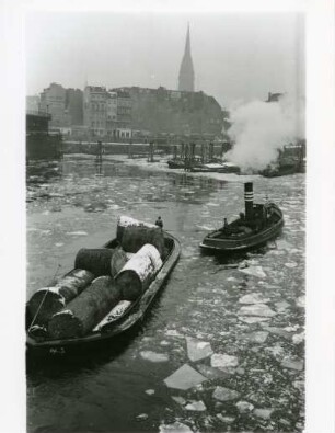 Der Hamburger Hafen im Winter. Ein Schlepper transportiert einen mit tropischen Edelhölzern beladenen Leichter durch das vereiste Hafenbecken