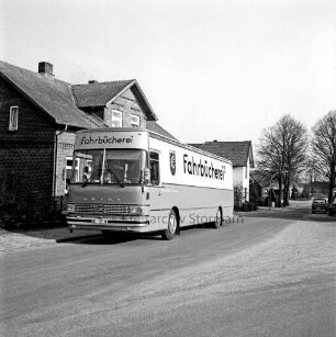 Bücherbus am Straßenrand vor Wohnhaus: im Hinterfgrund Straßenbäume, parkender Pkw