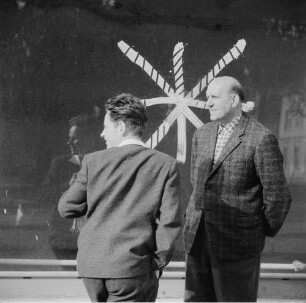 Niesky. Zwei Männer stehen vor einem Schaufenster, dessen Scheibe mit einem Farbkreuz markiert ist, und unterhalten sich