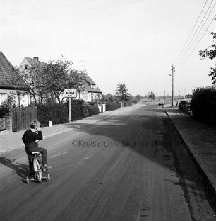 Fischbeker Straße: Kreisstraße in Richtung Fischbek: im Vordergrund links Kind mit Fahrrad: dahinter Siedlungshäuser mit Vorgärten und Ortsausgangsschild