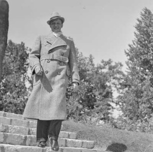 Mann in Hut und Mantel im Park vor einem Denkmal
