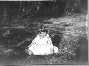 Photographien von Lappland. Kleines Mädchen mit Blütenkranz auf dem Kopf, auf einer Wiese sitzend