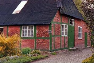 Floggensee (4): traufständige Fachwerkkate mit Blechdach: Giebelseite Wirtschaftstrakt mit Stalltür, rechts Abseite: davor Weg mit Kopfsteinpflaster, Vorgarten